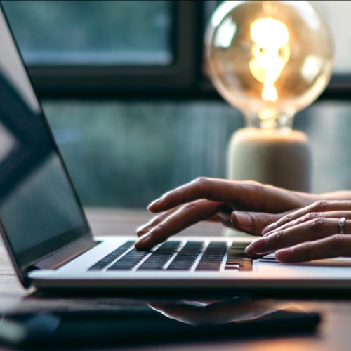 Person working on a laptop with a lightbulb in the background