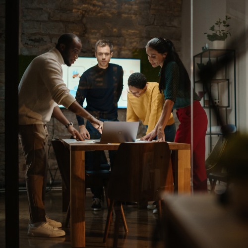 Four individuals standing and working together around a laptop